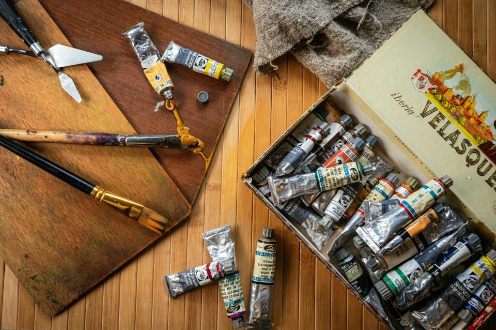 Foto de um ateliê com pincéis e tintas dispostos à uma mesa de madeira
