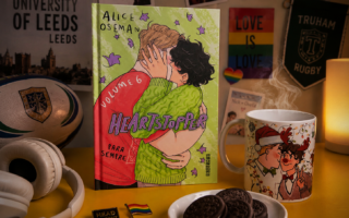 Volume 6 da série Heartstopper sobre a mesa com vários elementos que remetem ao universo.