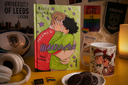 Volume 6 da série Heartstopper sobre a mesa com vários elementos que remetem ao universo.