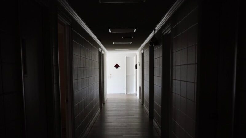 A dark and empty hallway indoors leading to a closed door, creating an eerie atmosphere.