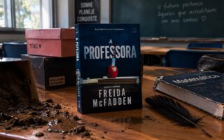 Capa do livro "A professora", de Freida McFadden com um fundo de sala de aula. Elementos presentes: caixas de sapato, lama e livros